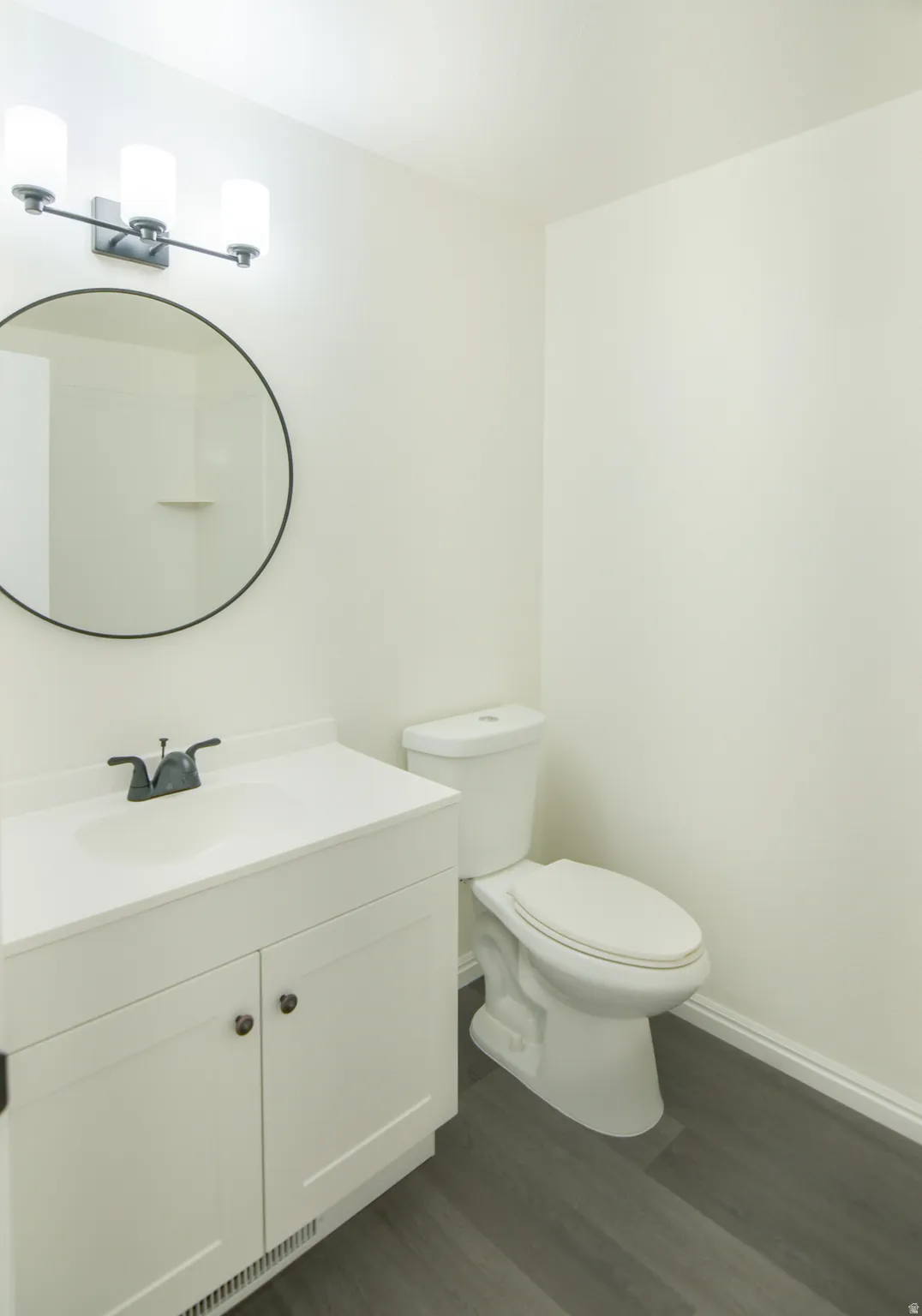 Bathroom featuring a white vanity with integrated sink, black-finish faucet, circular mirror, and three-light fixture