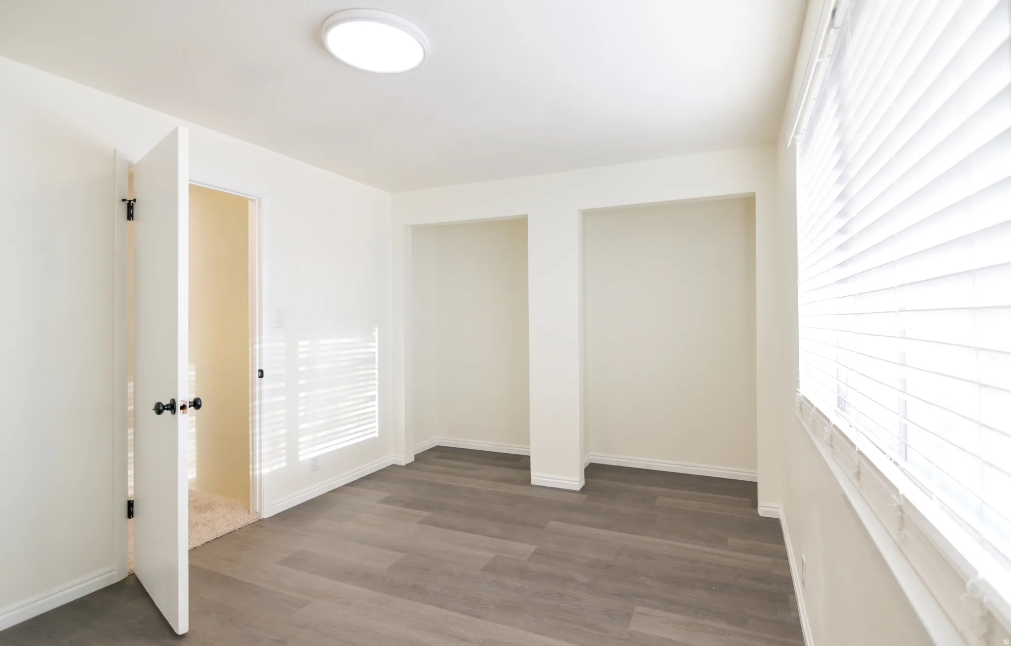 Room featuring wood-finish flooring, recessed wall niches, white baseboards, and a window with blinds