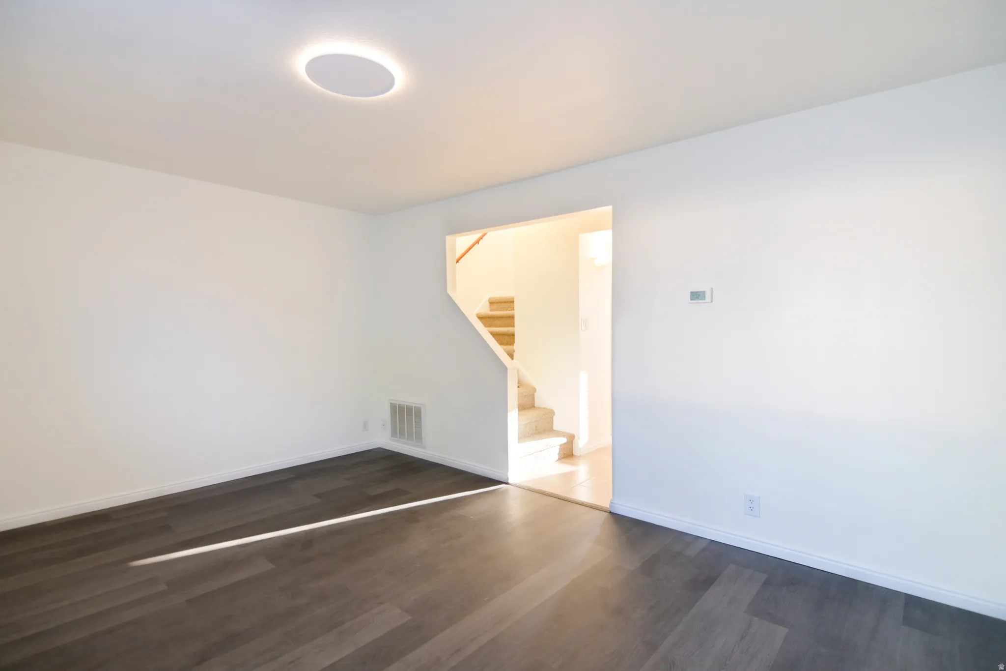 Spacious living area featuring dark wood-finish flooring, white baseboards, and a circular recessed ceiling light