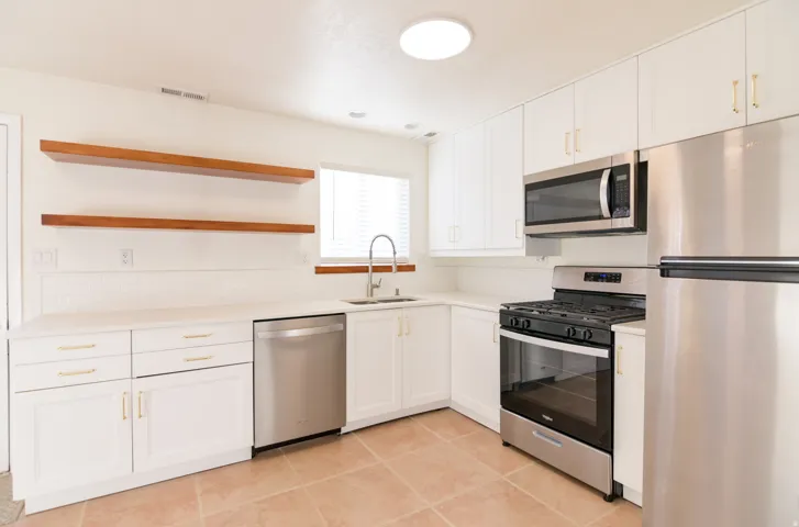 Kitchen featuring white cabinetry, stainless steel appliances, wood-finish open shelving, and light-toned countertops