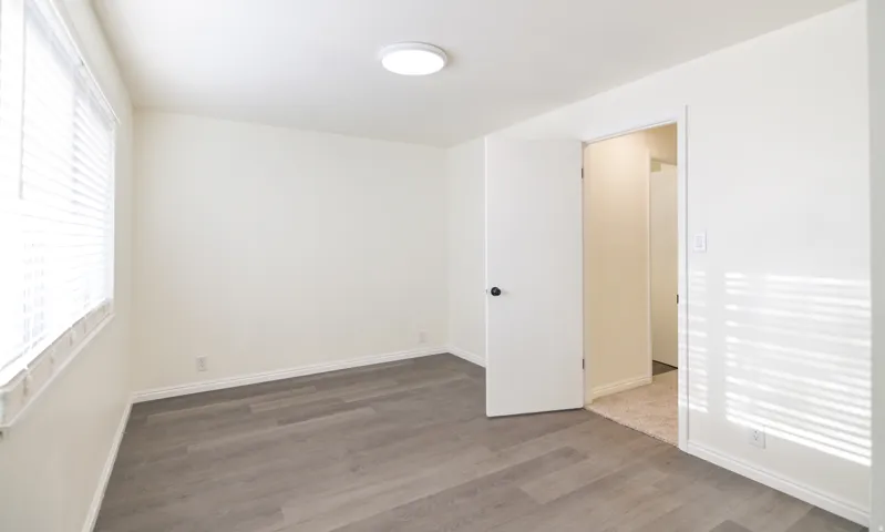 Spacious room featuring wood-finish flooring, white walls, and a ceiling-mounted light fixture