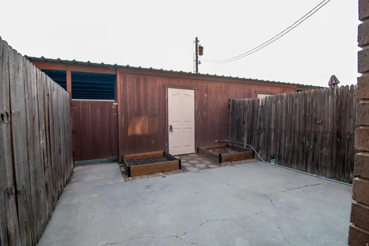 Concrete patio area bordered by a wood privacy fence and a wood-sided structure