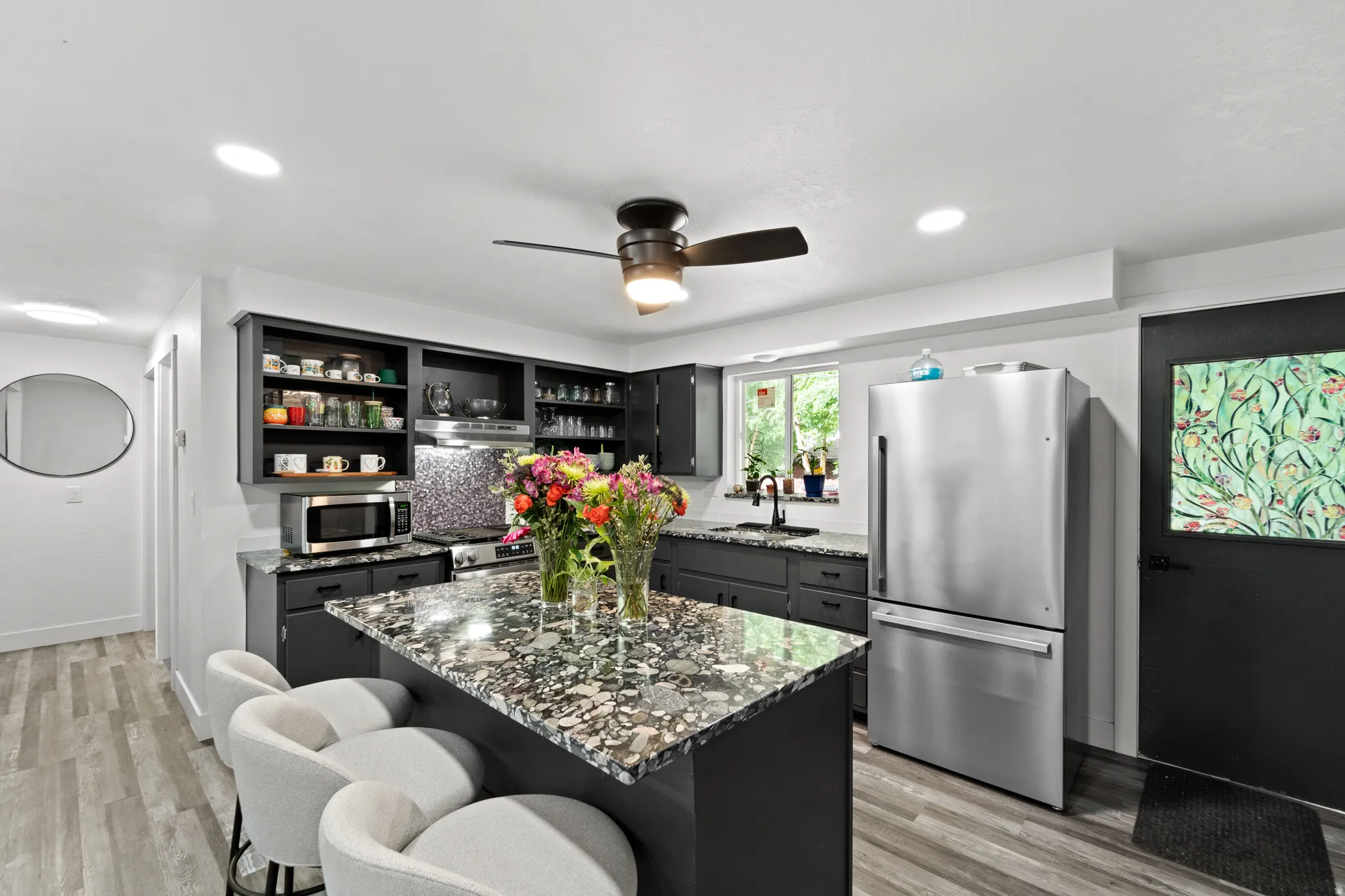 Modern kitchen featuring dark cabinetry, stainless steel appliances, and wood-finish flooring