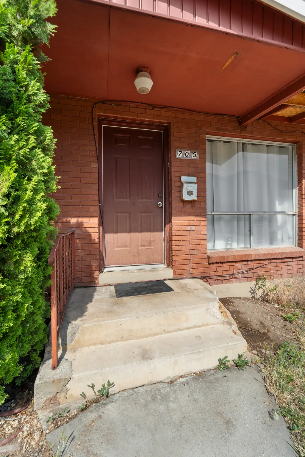 Brick exterior featuring a paneled entry door, concrete steps, and a metal handrail