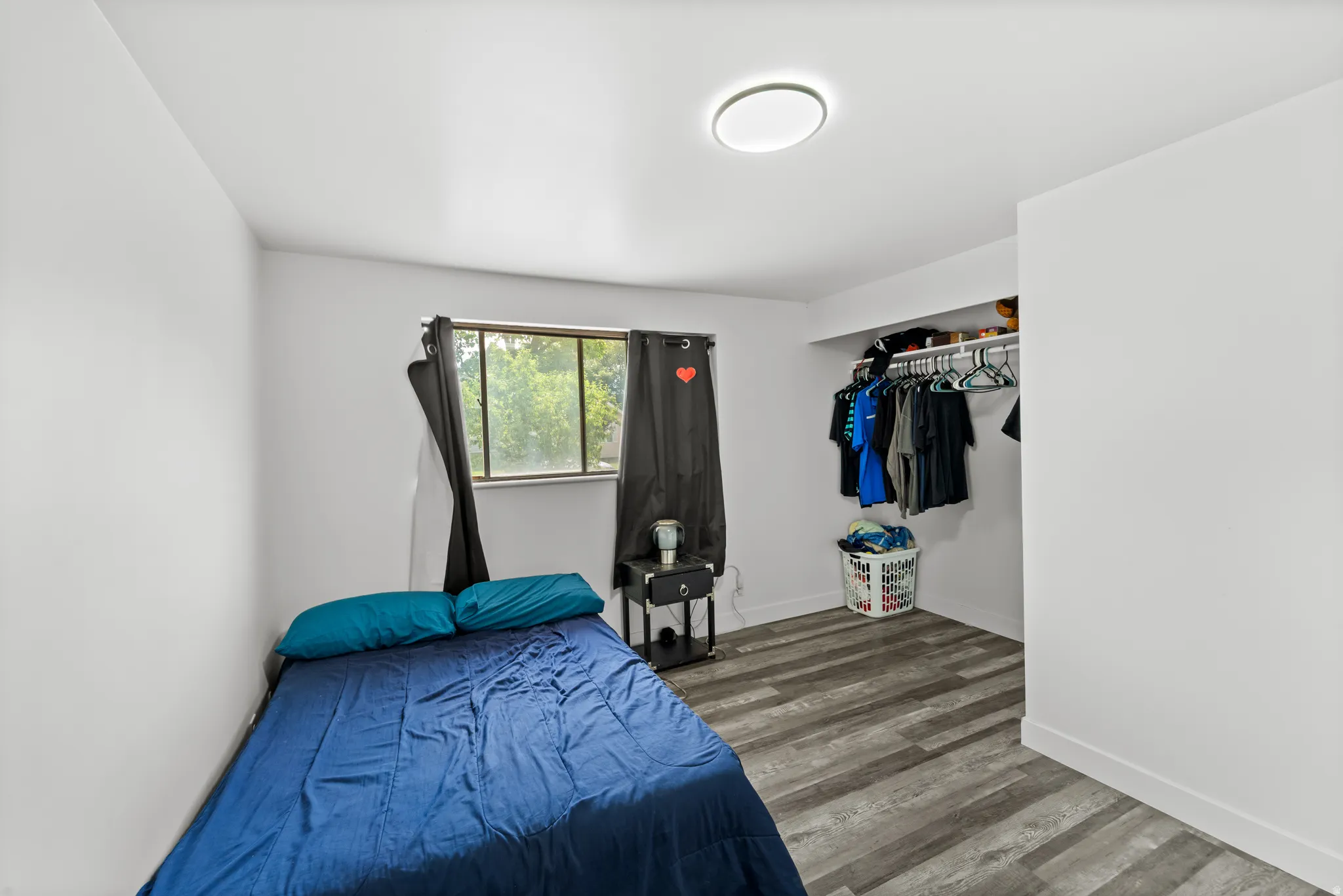 Interior room with light gray walls, wood-finish flooring, and a window with black privacy curtains