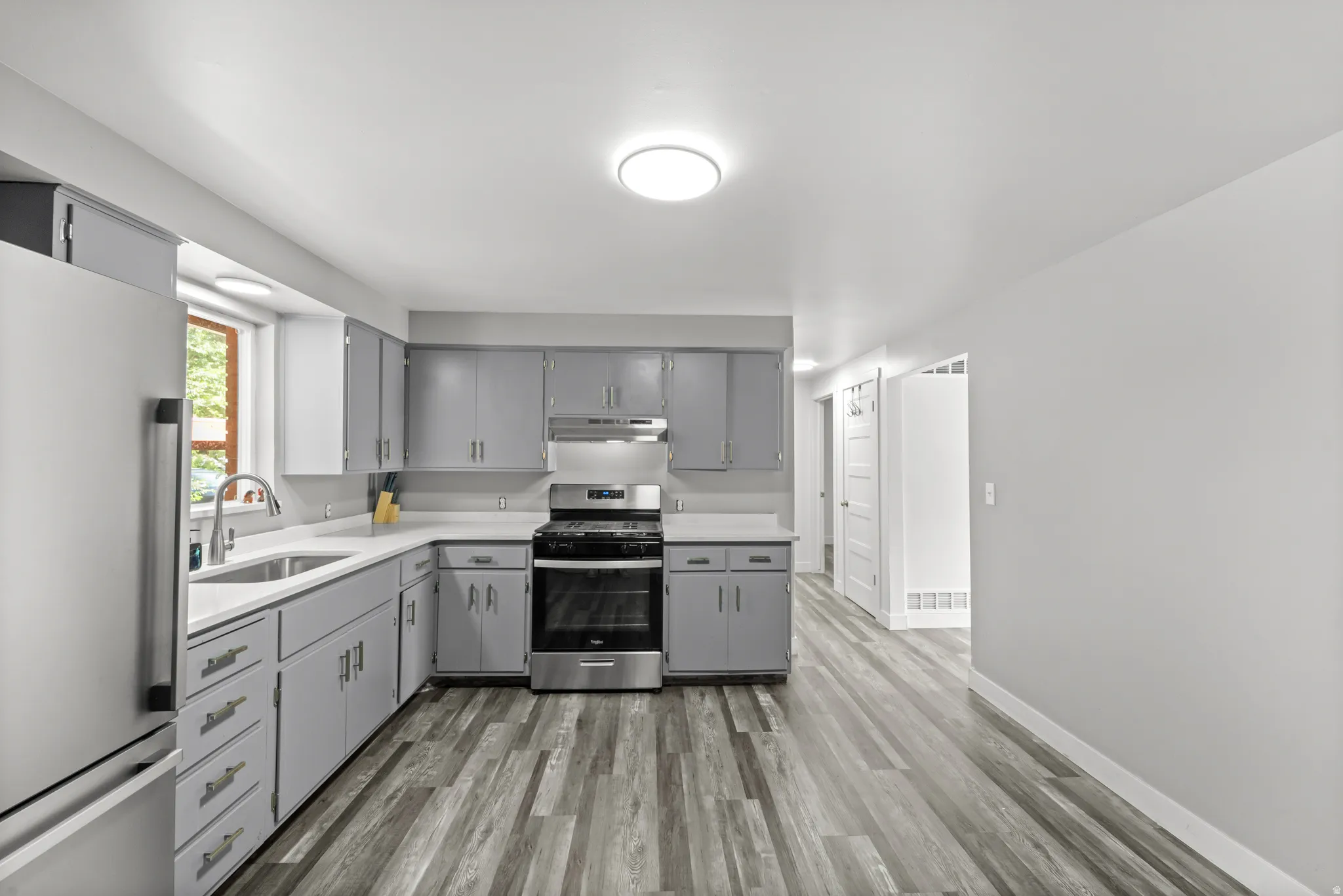 Modern kitchen featuring gray cabinetry, stainless steel appliances, light countertops, a stainless steel sink with a gooseneck faucet, and wood-finish flooring