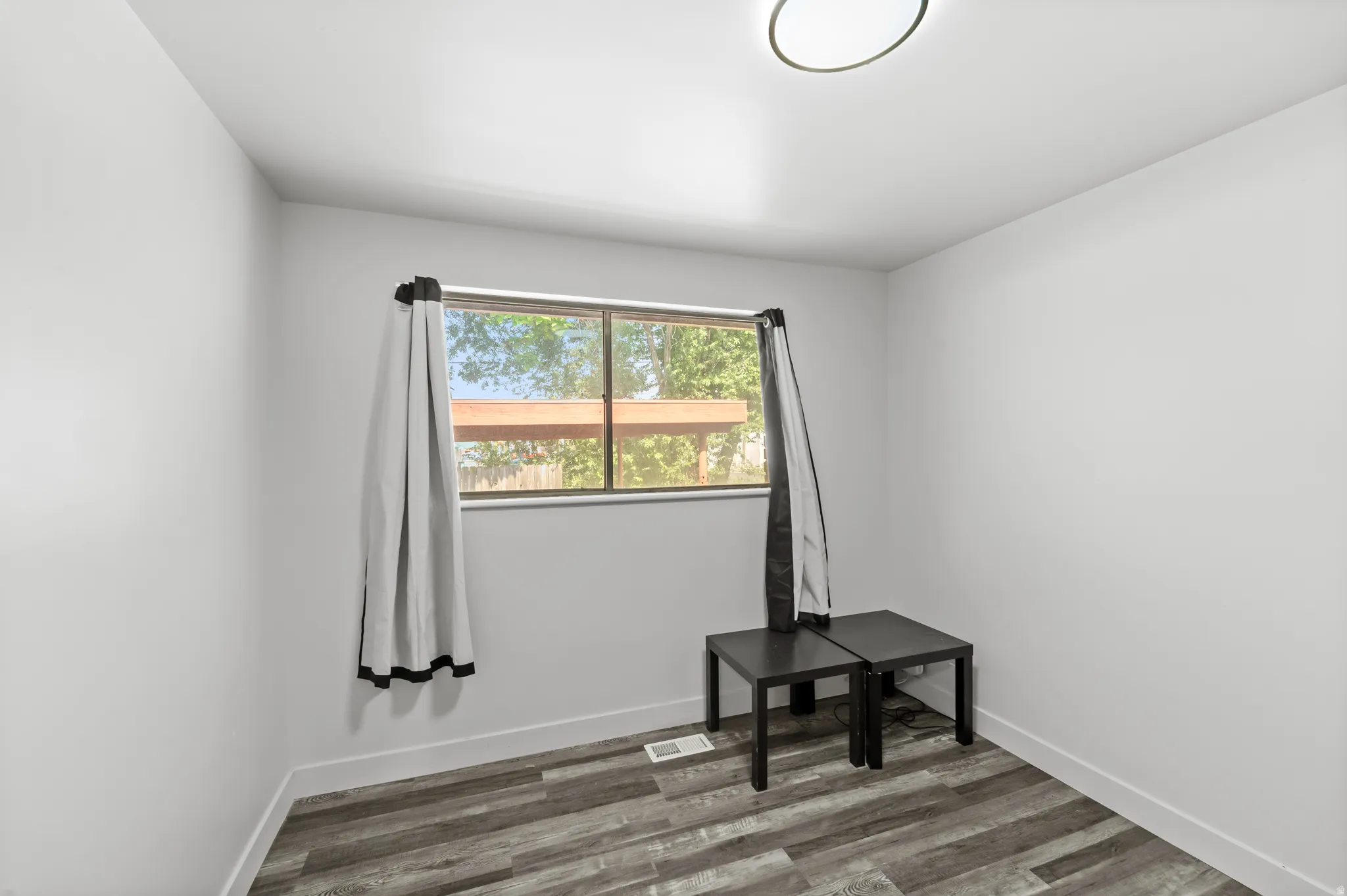 Room featuring wood-look flooring, a window with exterior views, white baseboards, and a flush-mount ceiling light