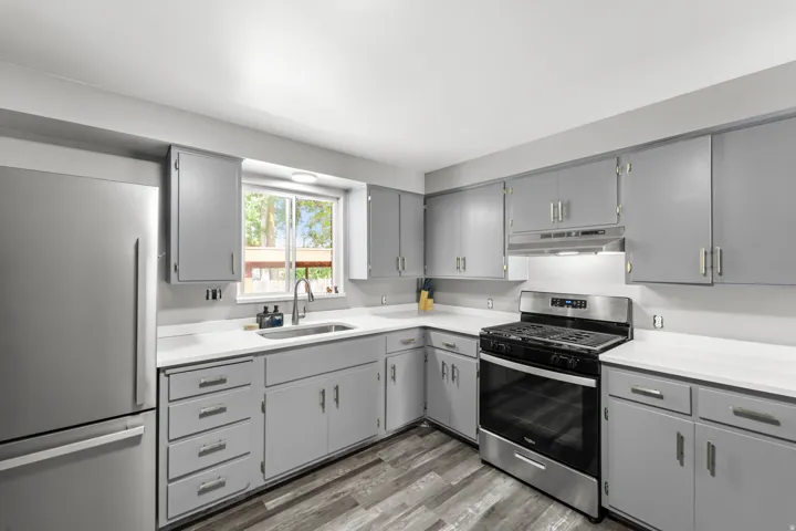 Kitchen featuring gray cabinetry, white countertops, stainless steel appliances, and wood-finish flooring