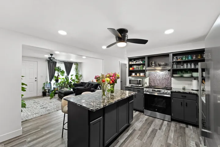 Kitchen featuring a central island with a granite-style countertop, stainless steel appliances, dark cabinetry, and wood-finish flooring