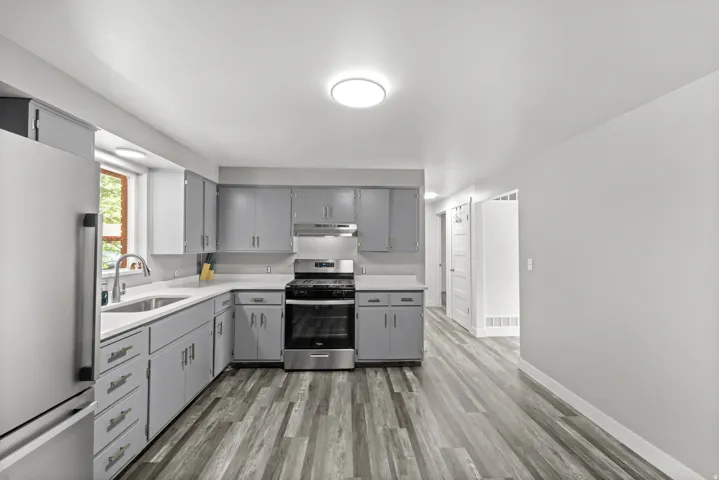 Modern kitchen featuring gray cabinetry, stainless steel appliances, light countertops, a stainless steel sink with a gooseneck faucet, and wood-finish flooring