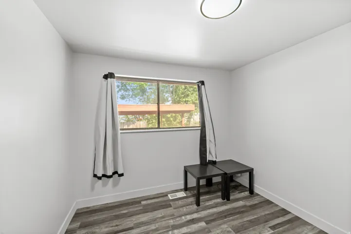 Room featuring wood-look flooring, a window with exterior views, white baseboards, and a flush-mount ceiling light