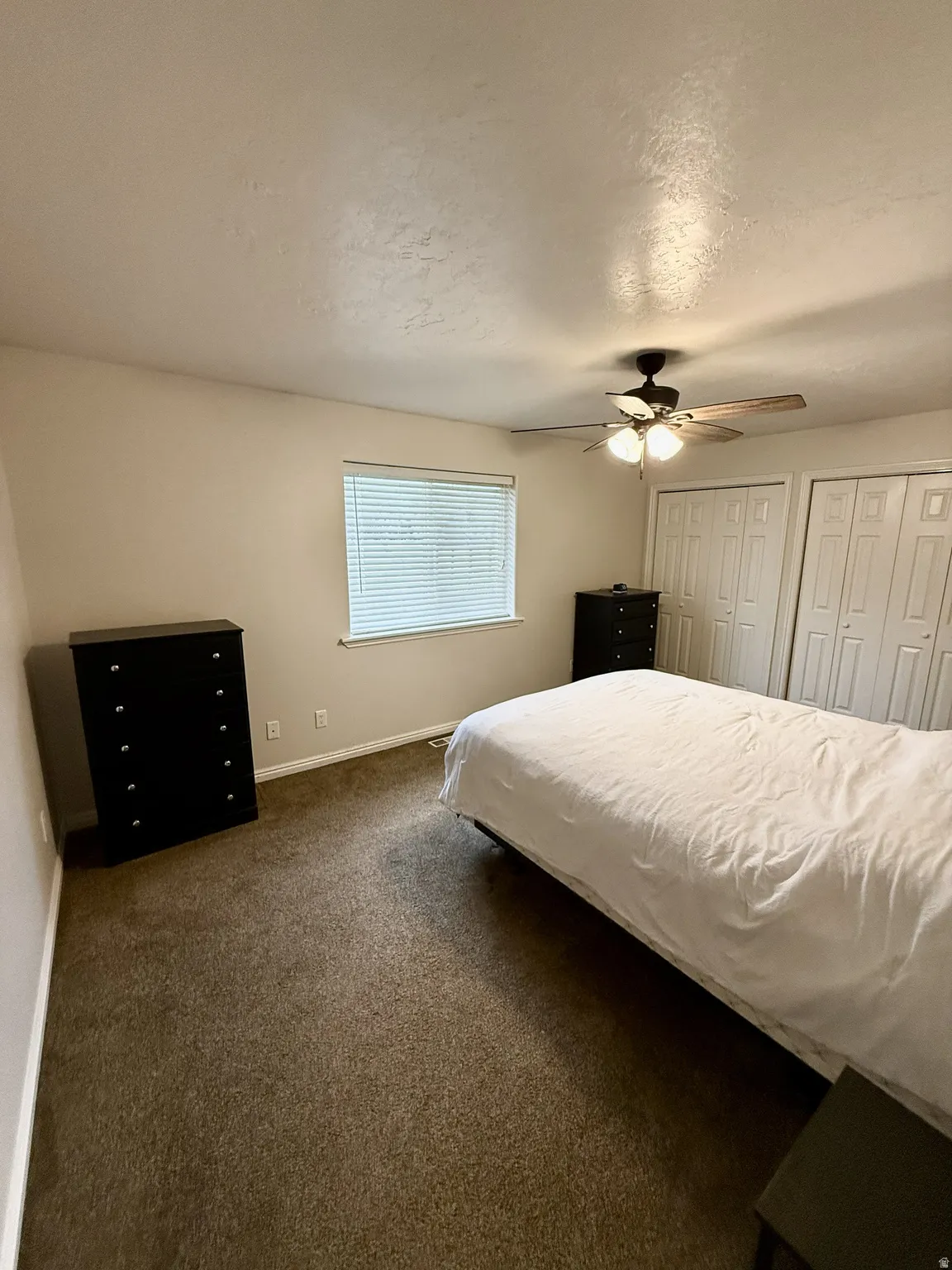 Carpeted room featuring a window with blinds, ceiling fan with integrated lighting, and dual bi-fold closet doors