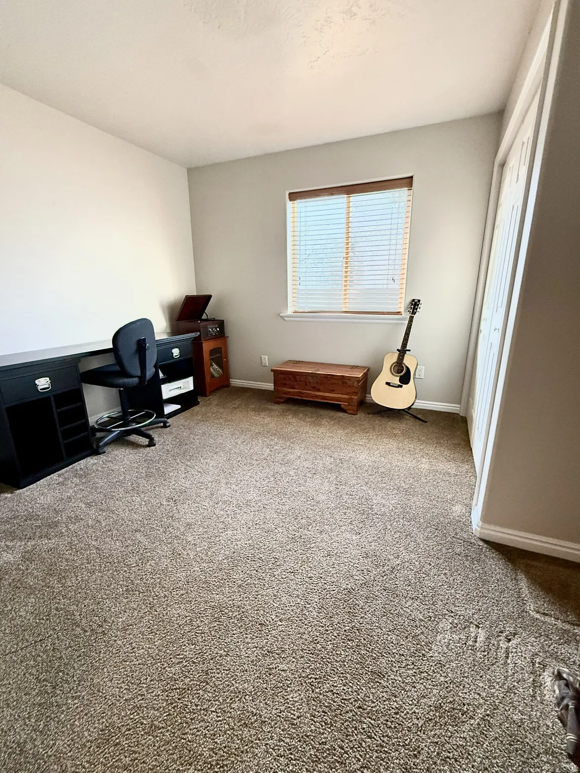 Neutral-toned carpeting extends throughout the room, complemented by a window with horizontal blinds and wood-finish trim