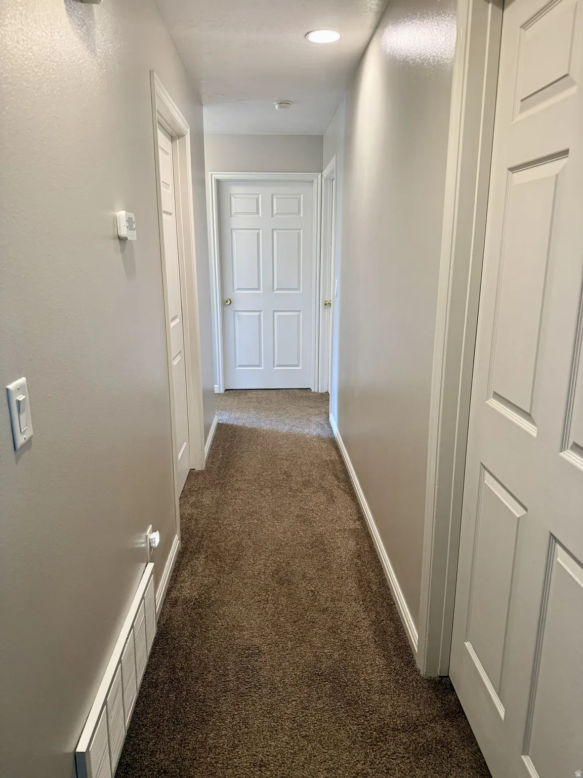 Carpeted hallway with light gray walls, recessed lighting, and white paneled doors