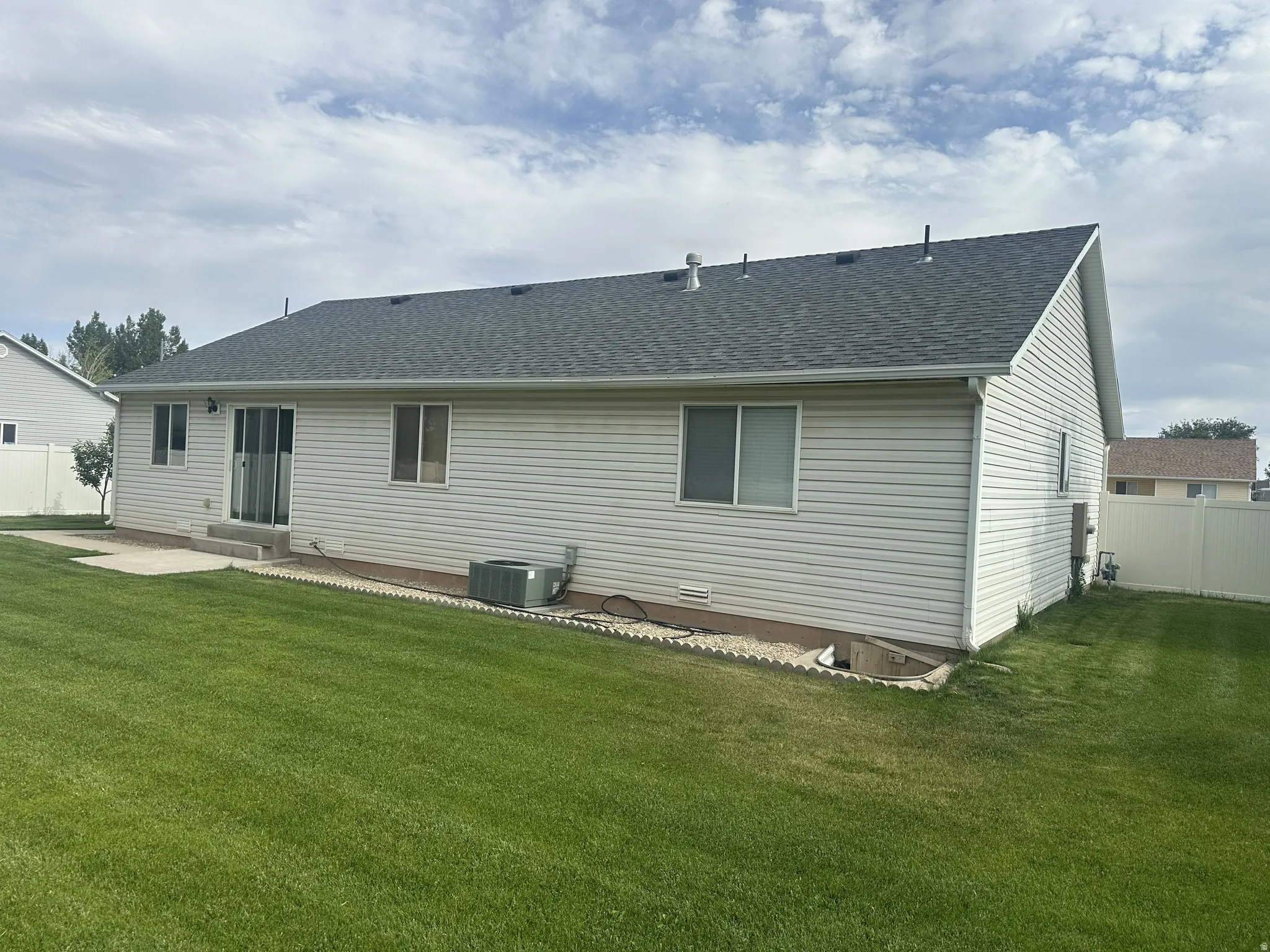 Expansive backyard featuring a manicured lawn, concrete patio, and white vinyl siding