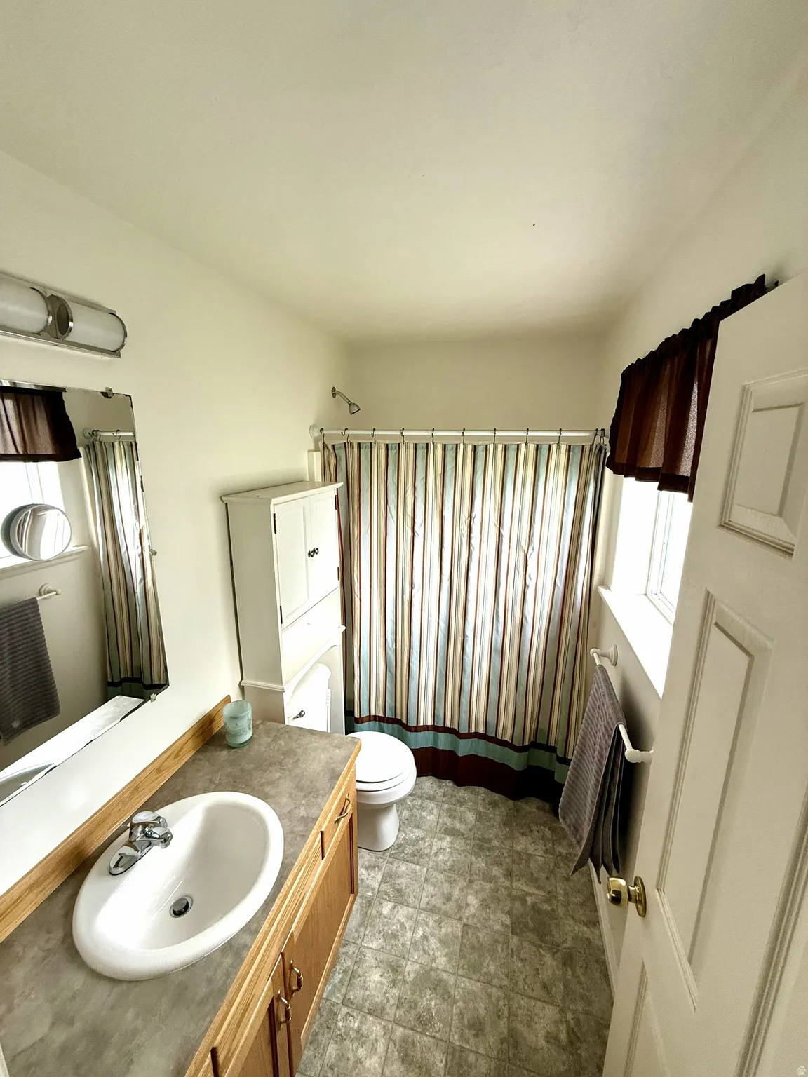 Full bathroom featuring a single vanity with a laminate countertop, light wood-finish cabinetry, and a white oval sink