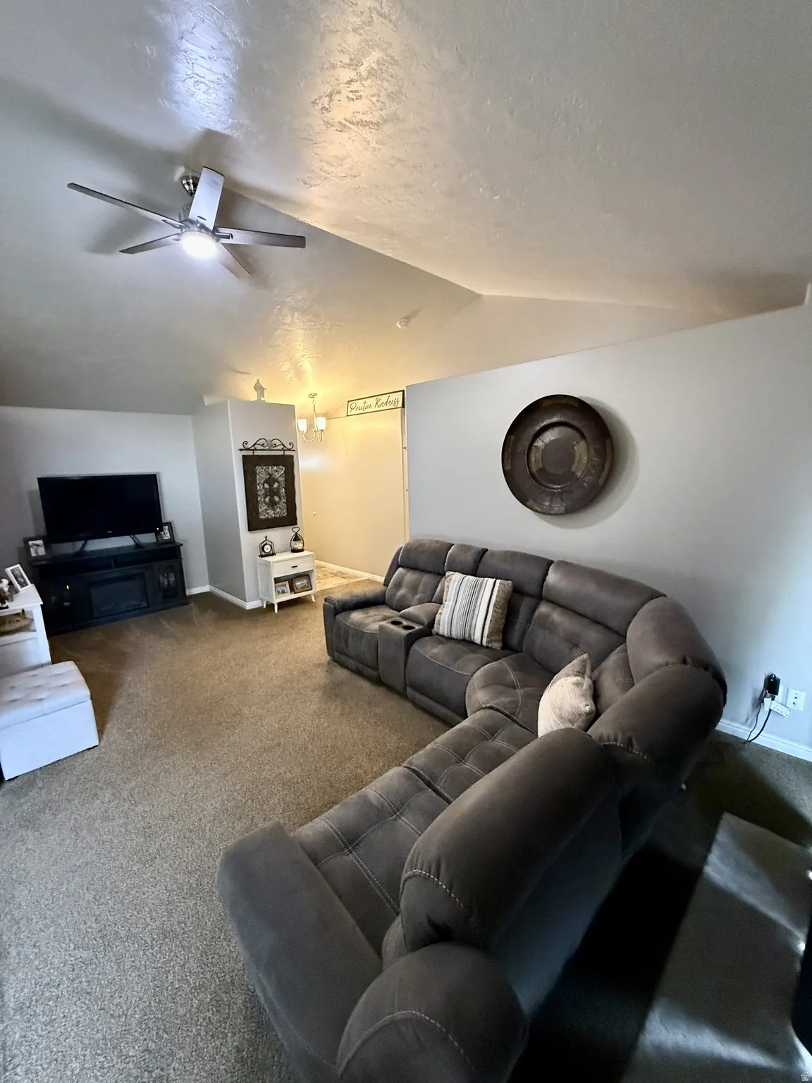 Spacious living area featuring vaulted ceilings, a ceiling fan with integrated lighting, and neutral carpeting