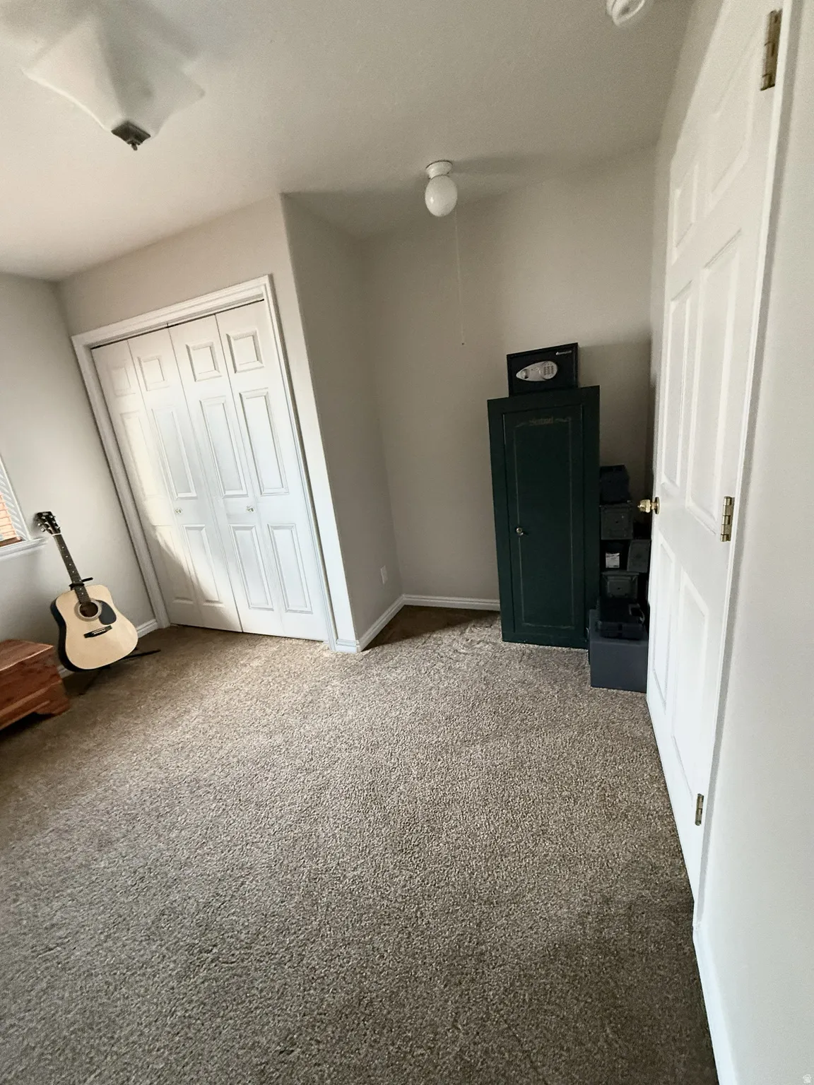 Plush carpeting fills this room featuring neutral wall tones, a flush-mount ceiling light, and ample closet storage behind bi-fold paneled doors