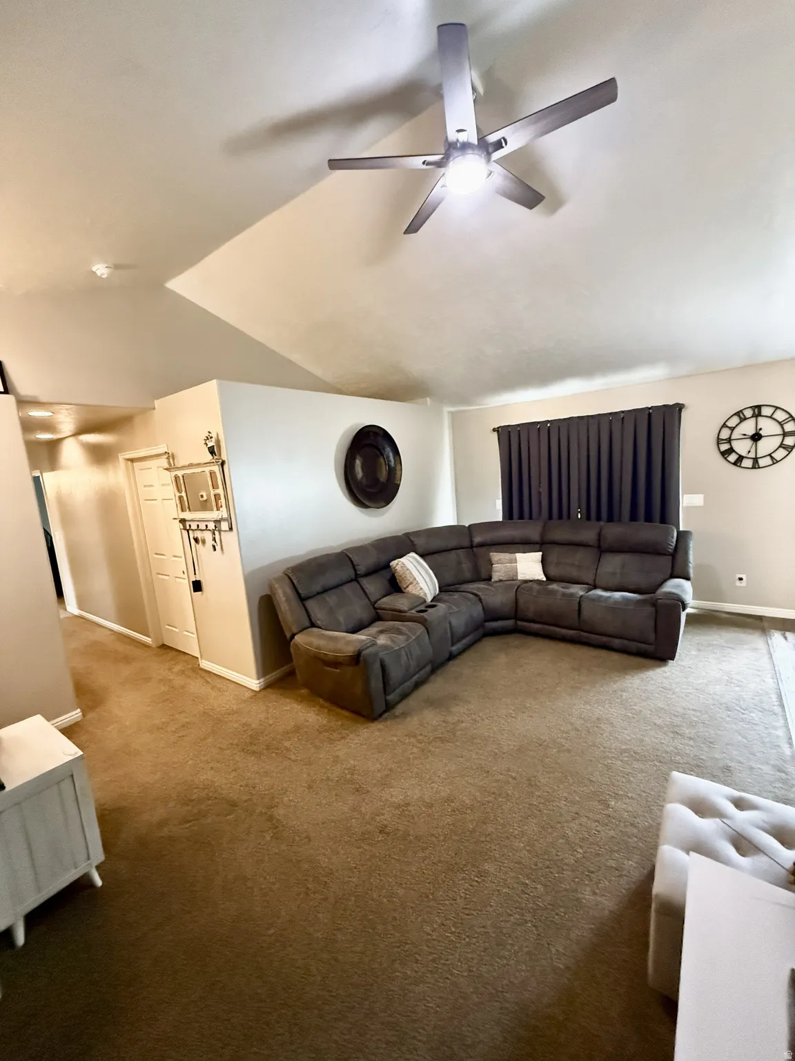 Living area featuring vaulted ceilings, a ceiling fan with integrated lighting, and neutral-toned carpeting throughout