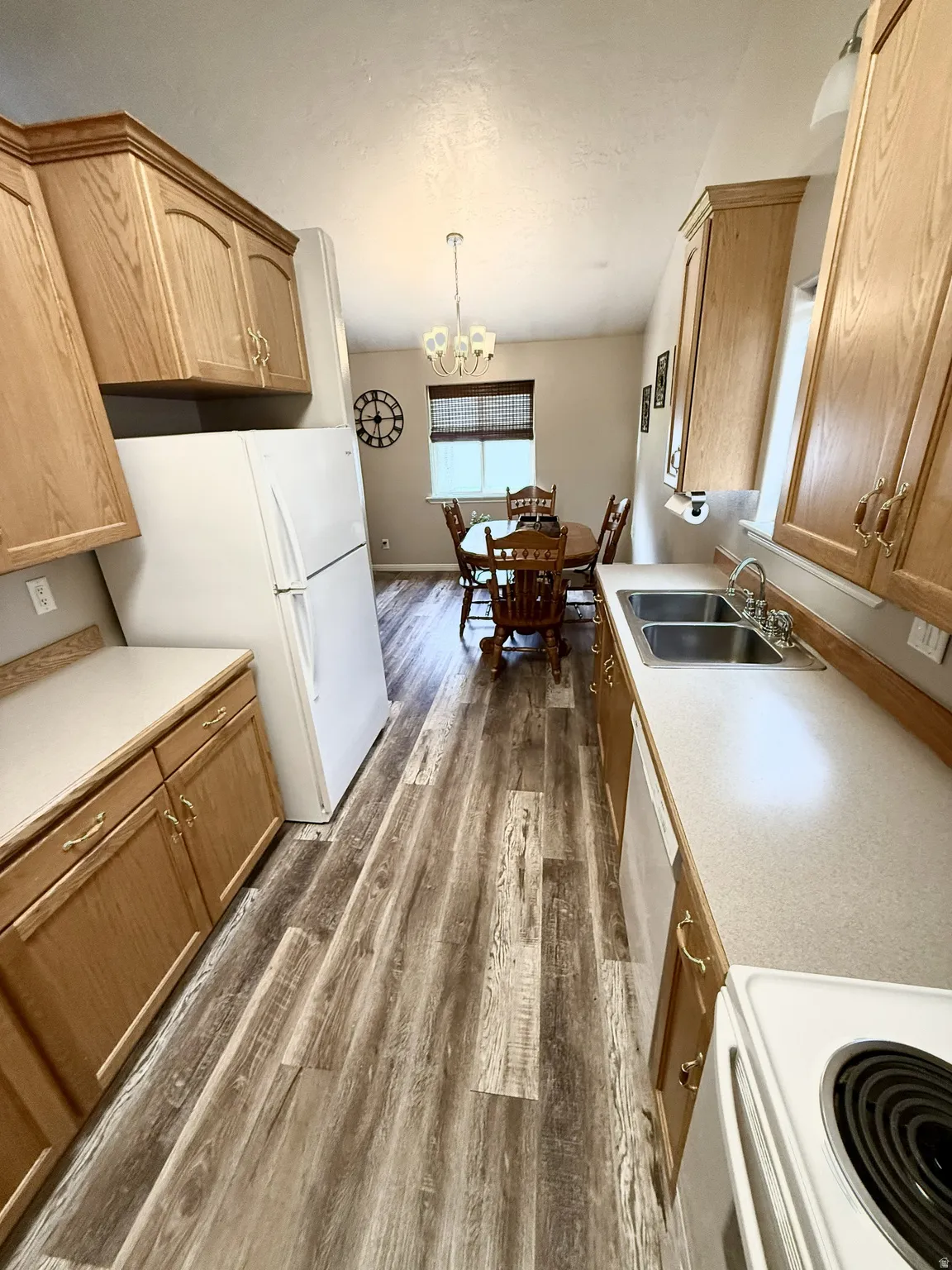 Galley kitchen featuring wood-finish flooring, light wood cabinetry with brass-tone hardware, and light-toned countertops