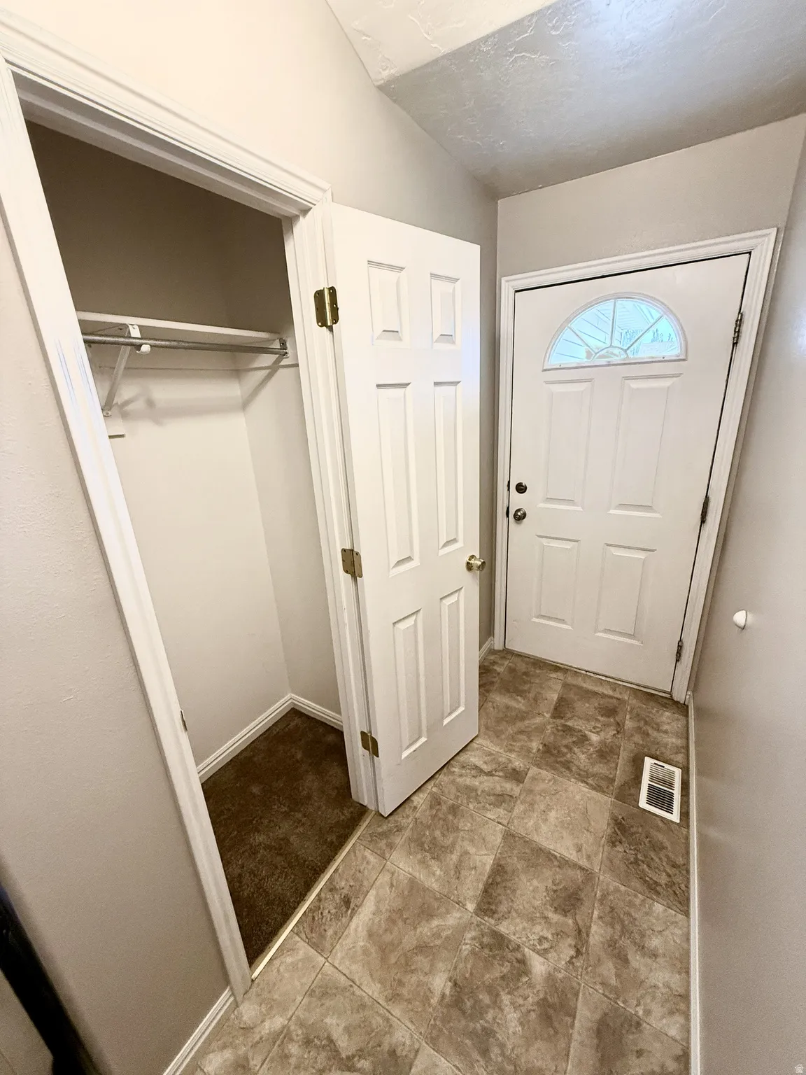 Entryway featuring a white paneled door with an arched glass insert, a built-in coat closet with shelving, and neutral-toned tile flooring