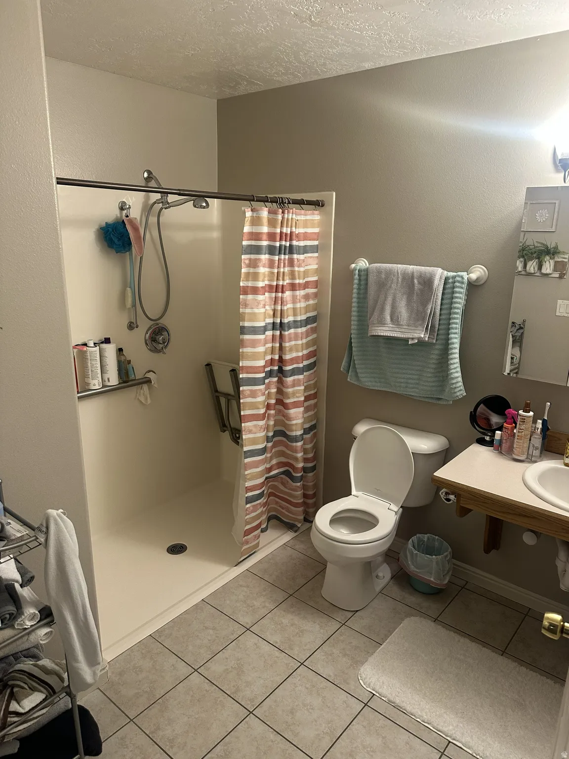Bathroom featuring a walk-in shower with grab bars, a single vanity with a laminate countertop, a toilet, and tiled flooring