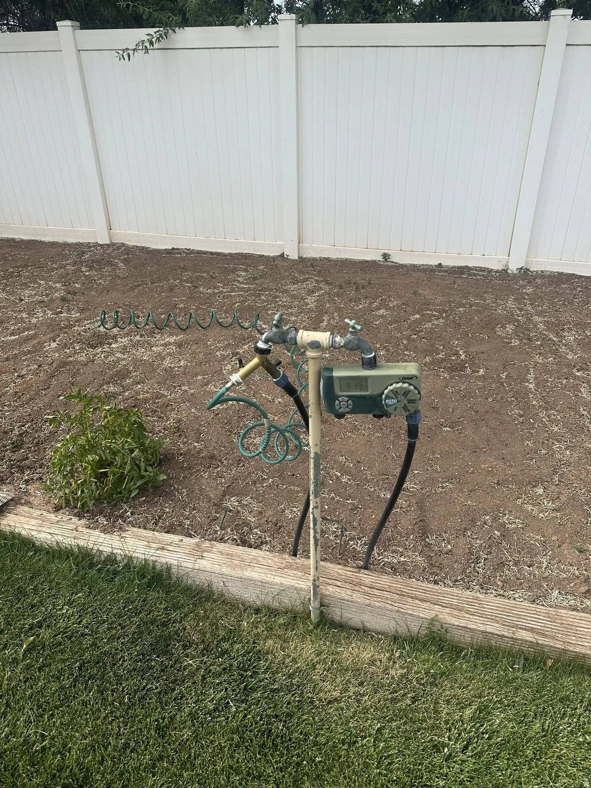 White privacy fence enclosing a tilled garden area with a dedicated spigot and hose connection