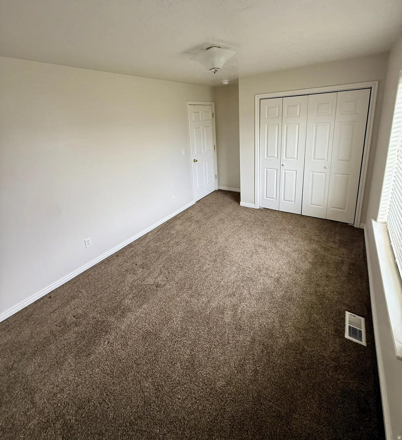 Spacious room featuring brown carpeting, light neutral wall color, and white trim