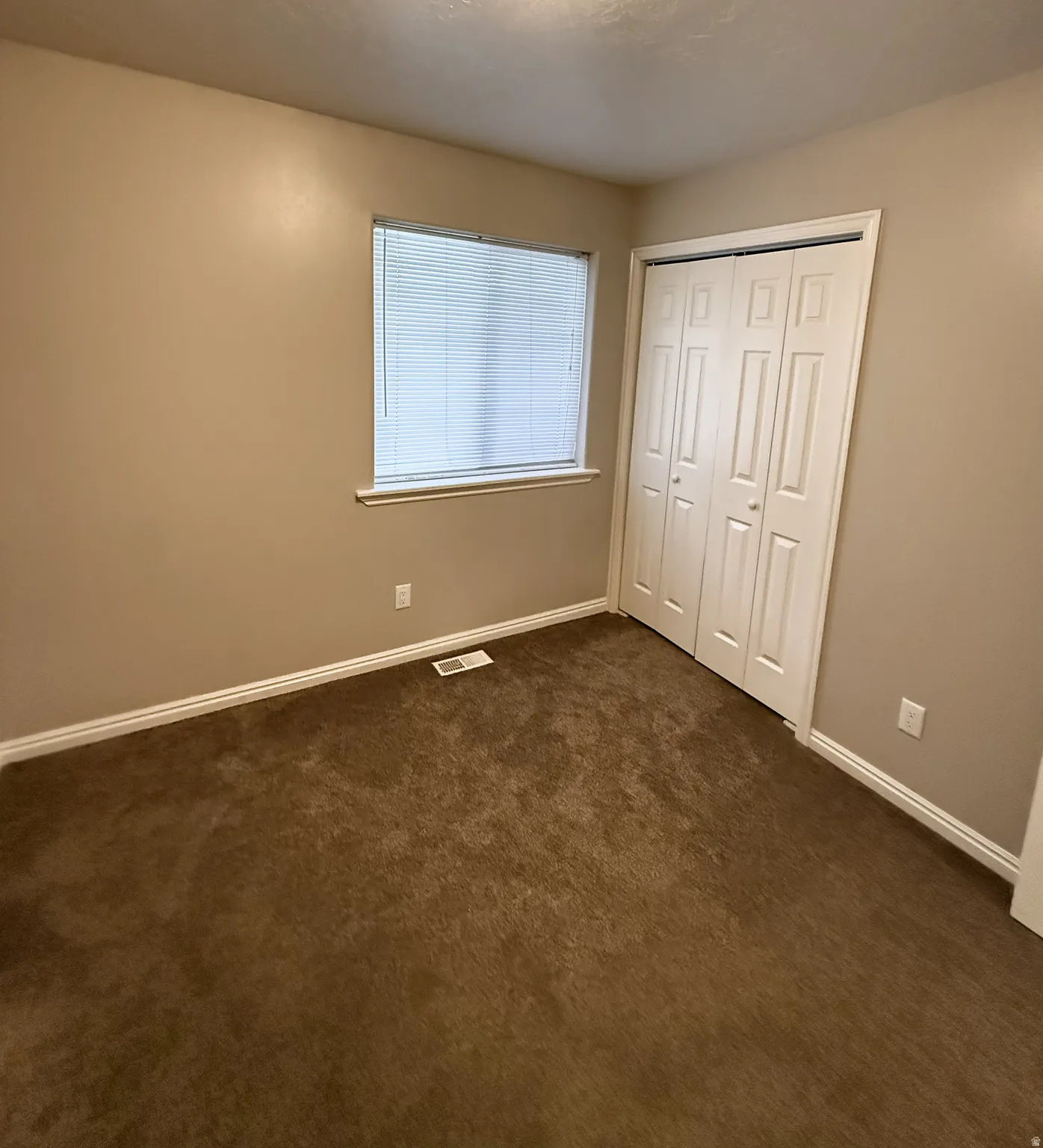 Carpeted room featuring a window with horizontal blinds, bi-fold closet doors, and white baseboards