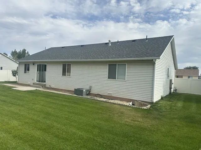 Expansive backyard featuring a manicured lawn, concrete patio, and white vinyl siding