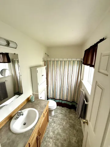 Full bathroom featuring a single vanity with a laminate countertop, light wood-finish cabinetry, and a white oval sink