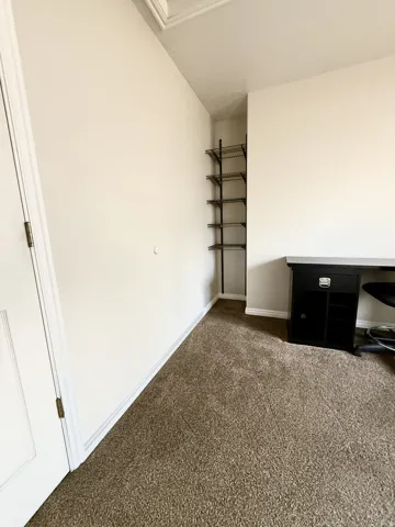 Room featuring wall-to-wall carpeting, light neutral wall paint, and a built-in shelving unit