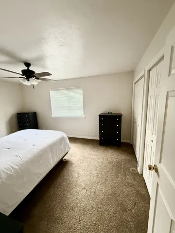 Carpeted room featuring a ceiling fan with integrated lighting, a window with horizontal blinds, and bi-fold closet doors