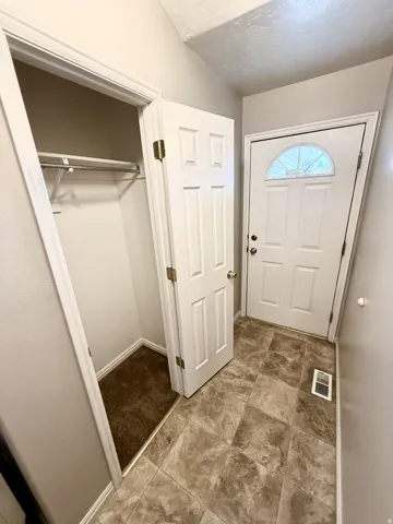 Entryway featuring a white paneled door with an arched glass insert, a built-in coat closet with shelving, and neutral-toned tile flooring