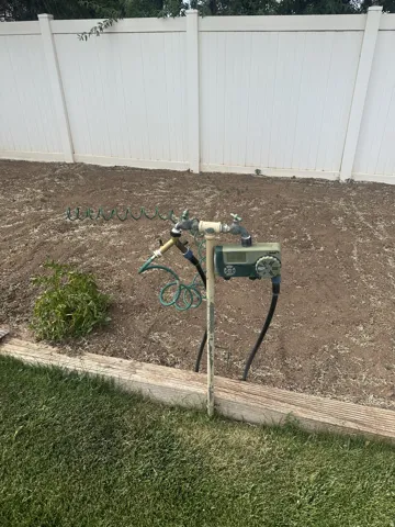 White privacy fence enclosing a tilled garden area with a dedicated spigot and hose connection