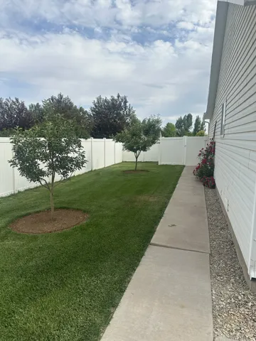 Expansive backyard featuring a manicured lawn, two young trees, and full white vinyl fencing
