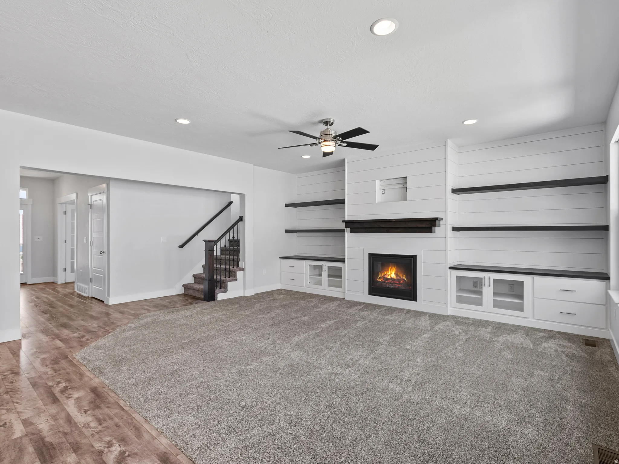 Carpeted living area featuring a fireplace with shiplap surround, built-in shelving and cabinetry, recessed lighting, and wood-finish flooring