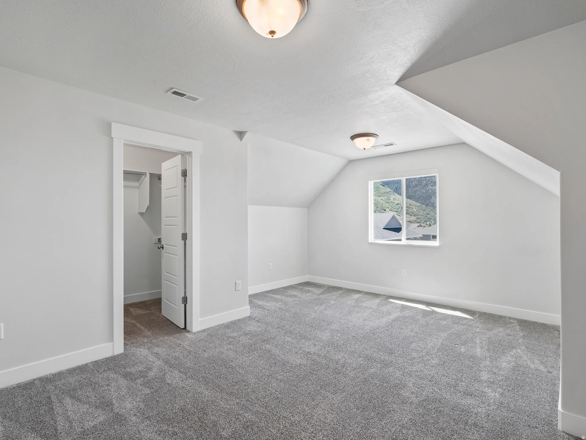 Carpeted room featuring a white interior door, a single window, and sloped ceiling details