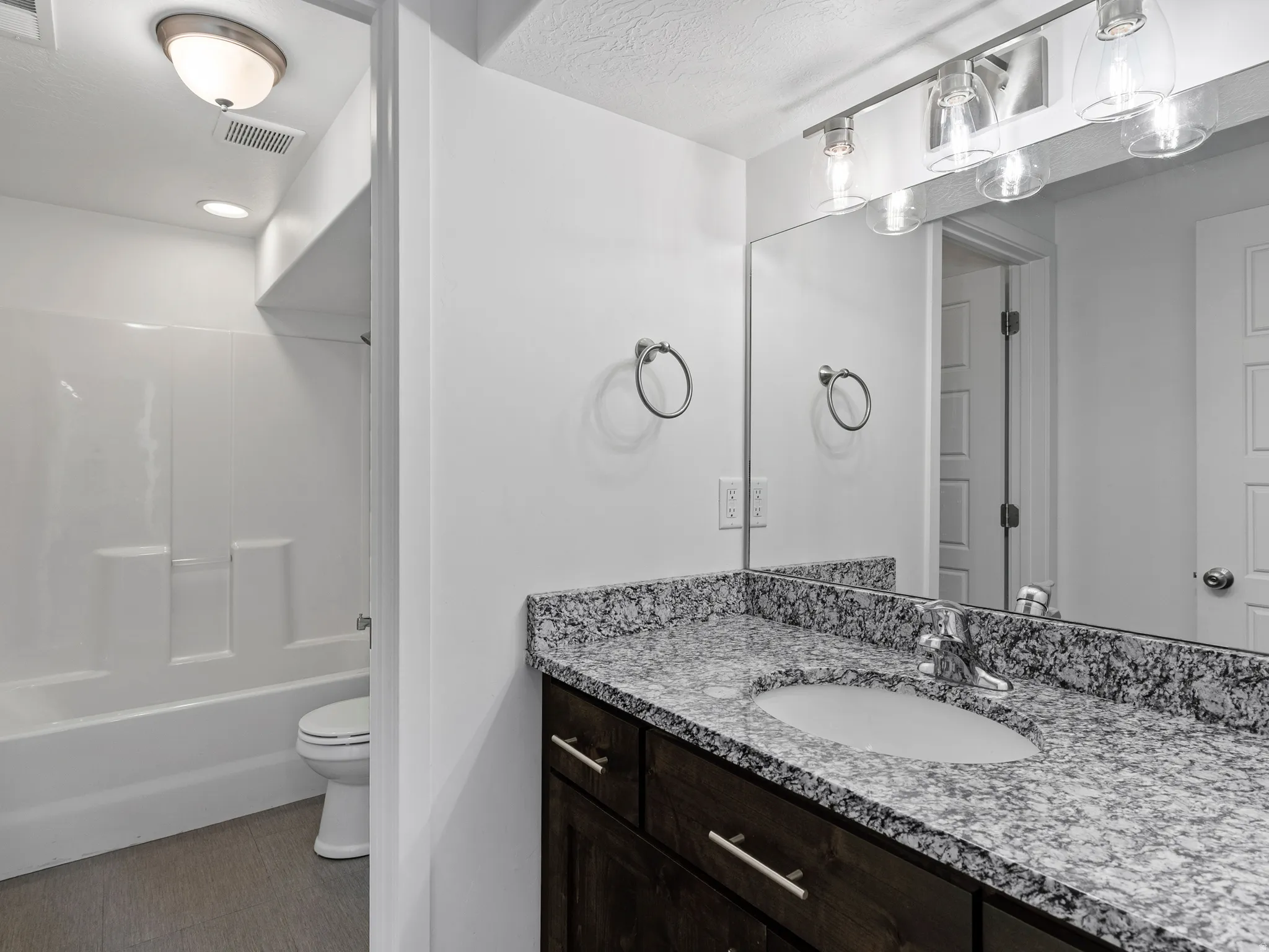 Bathroom featuring a dark wood-finish vanity with a light speckled countertop, an integrated sink, and a large mirror