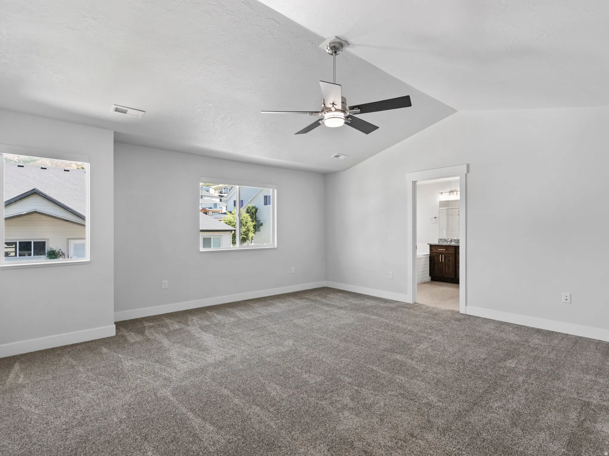Spacious room featuring vaulted ceilings, a ceiling fan with integrated lighting, and two windows