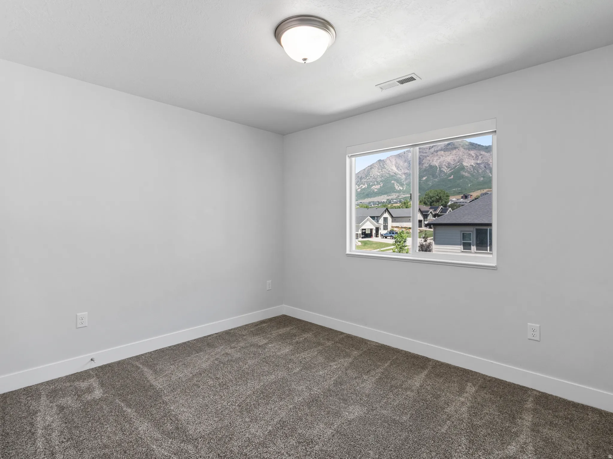 Interior space featuring neutral wall paint, gray patterned carpeting, a white trim baseboard, and a window with a mountain backdrop