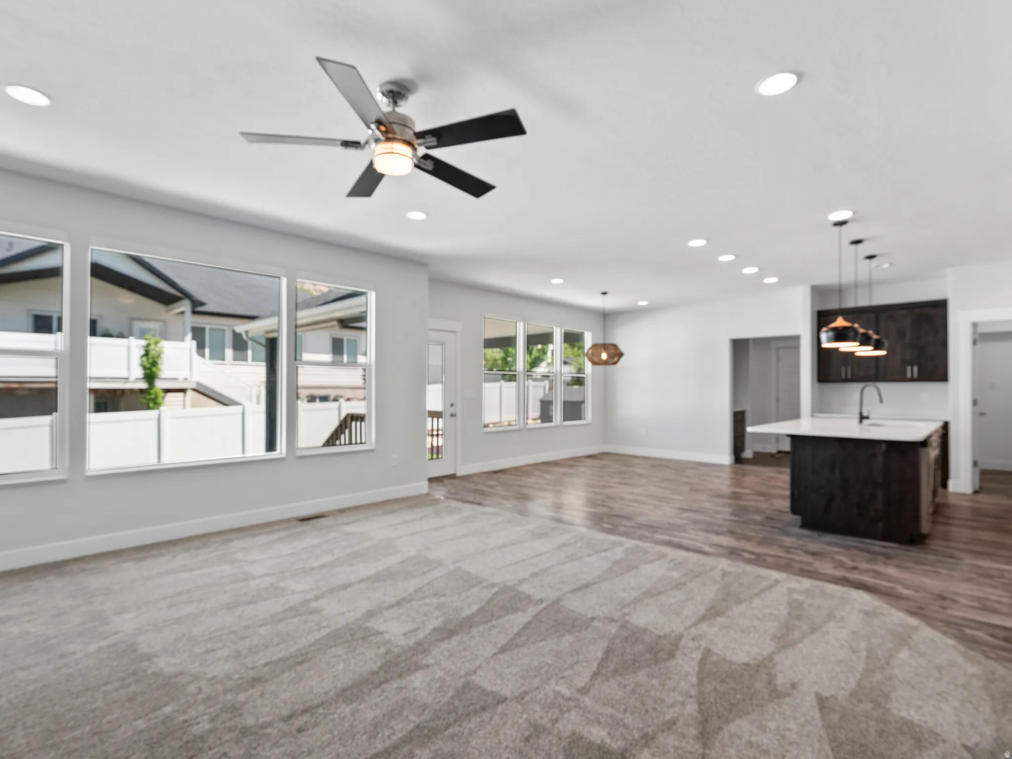 Open-concept living space featuring a gray patterned carpet, wood-finish flooring, a kitchen island with pendant lighting, and multiple windows