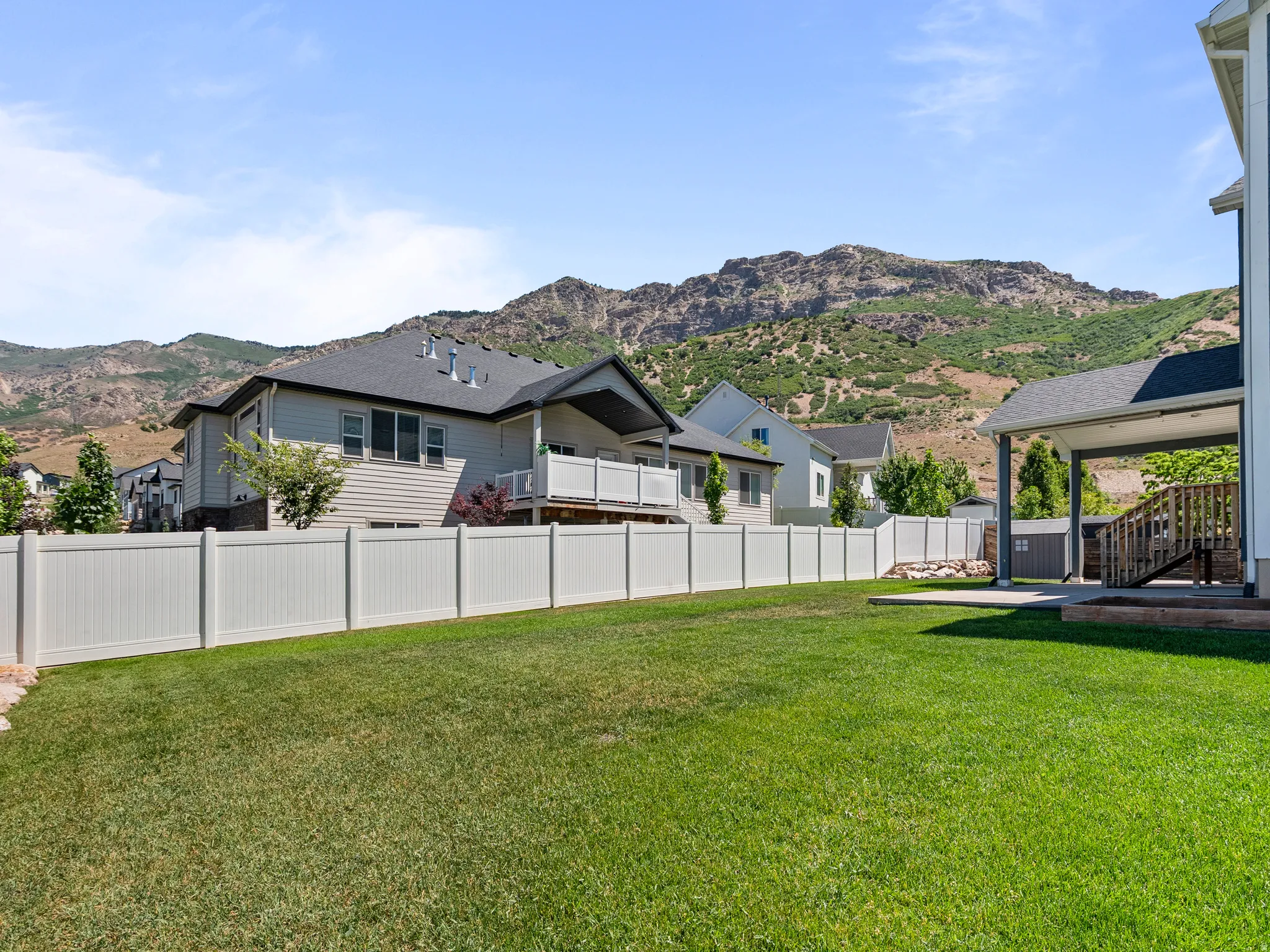 Expansive backyard featuring a manicured lawn, full privacy fencing, and a covered patio area with a wood deck