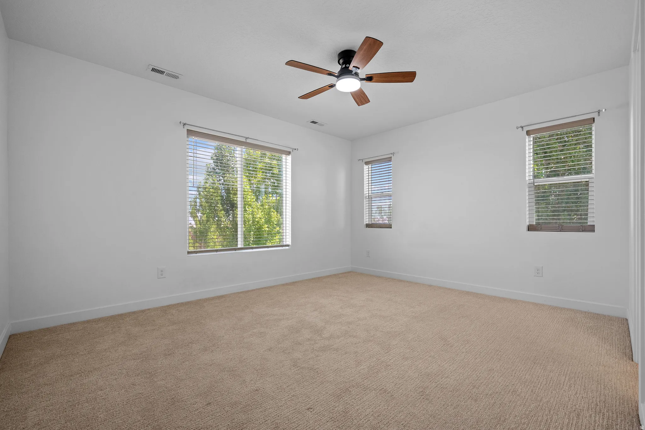 Bright interior space featuring light-colored carpeting and multiple windows with blinds