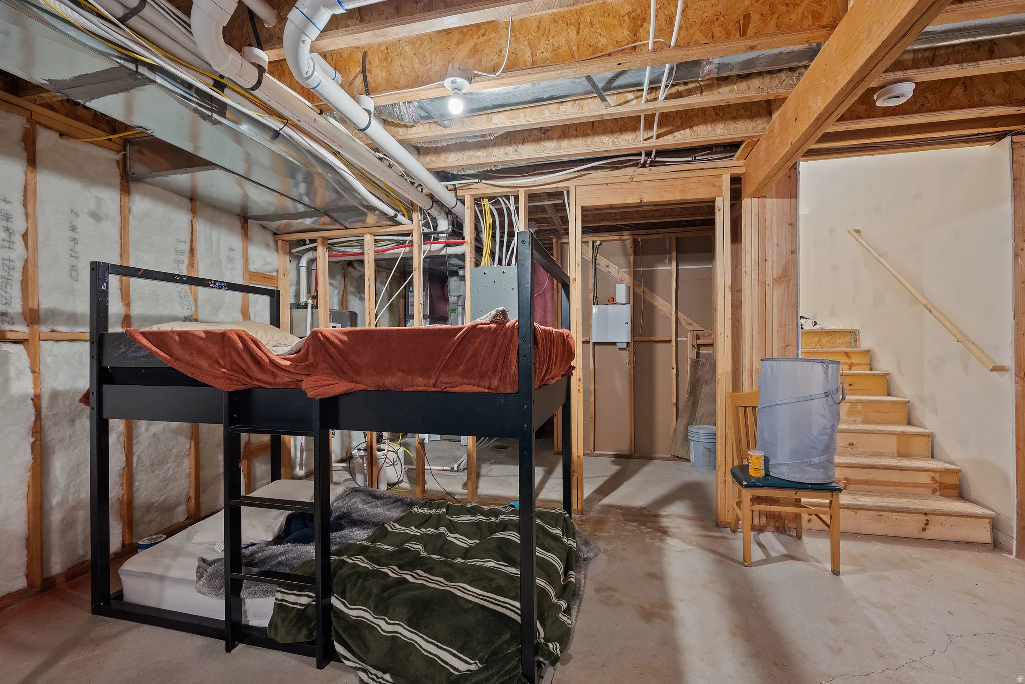 Unfinished basement space featuring exposed joists, visible insulation, and concrete flooring