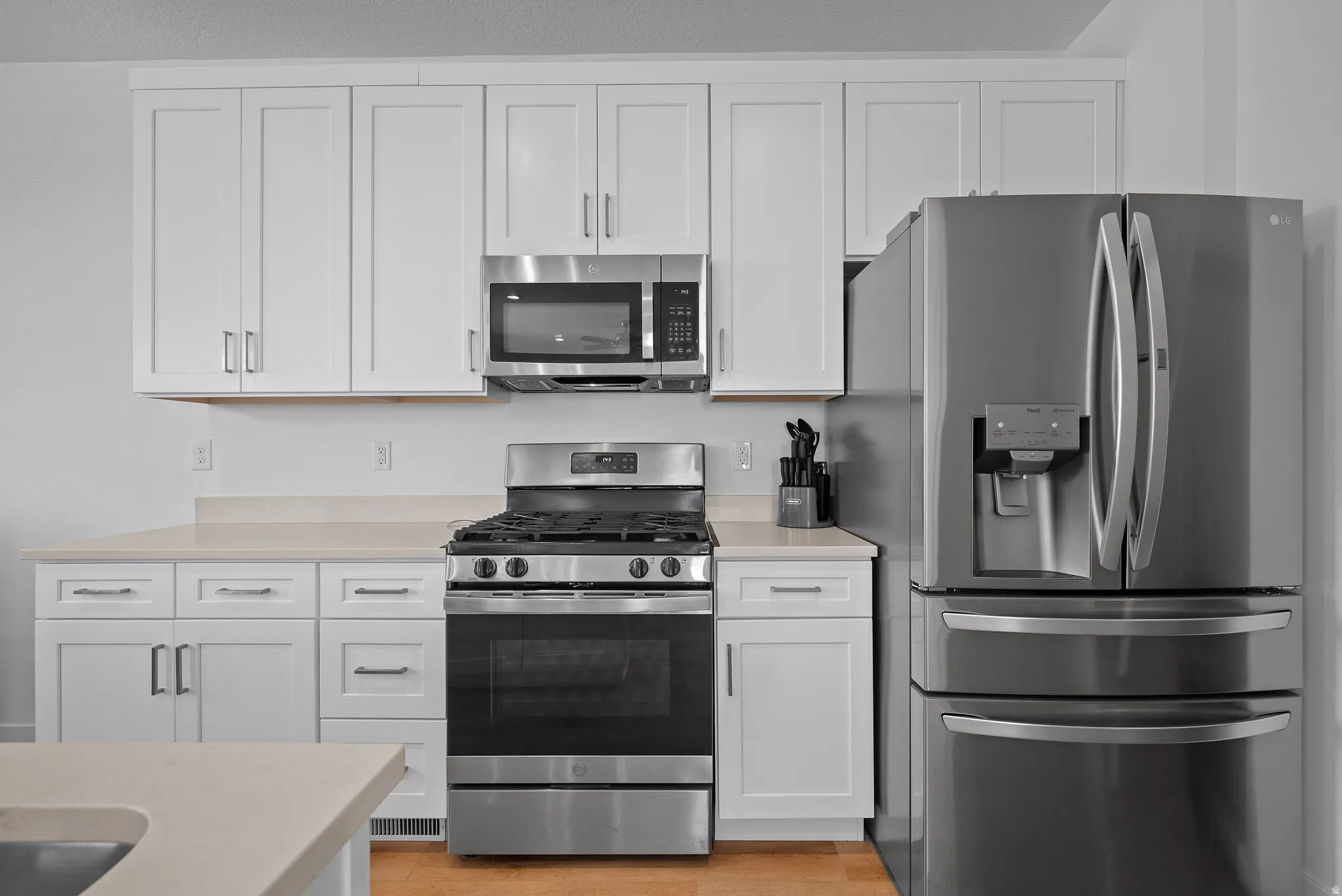 Kitchen featuring white shaker cabinetry, light-toned countertops, stainless steel appliances, and wood-finish flooring