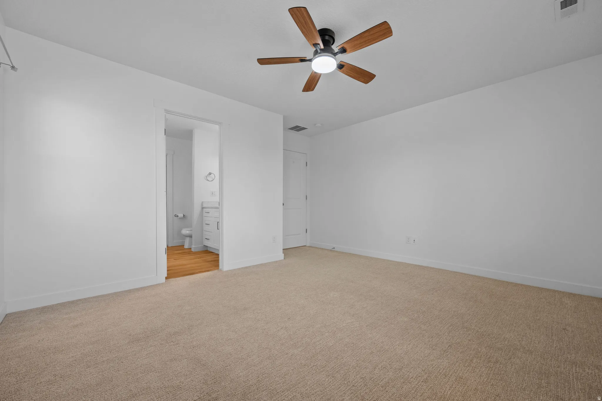 Carpeted room featuring a ceiling fan with wood-finish blades, white walls, and white baseboards