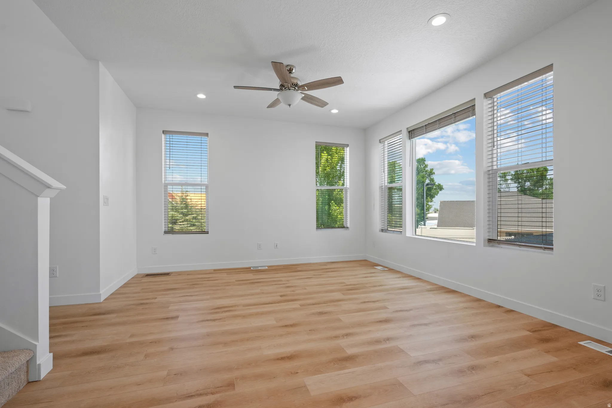 Spacious room featuring wood-finish flooring, multiple windows with blinds, a ceiling fan, and recessed lighting