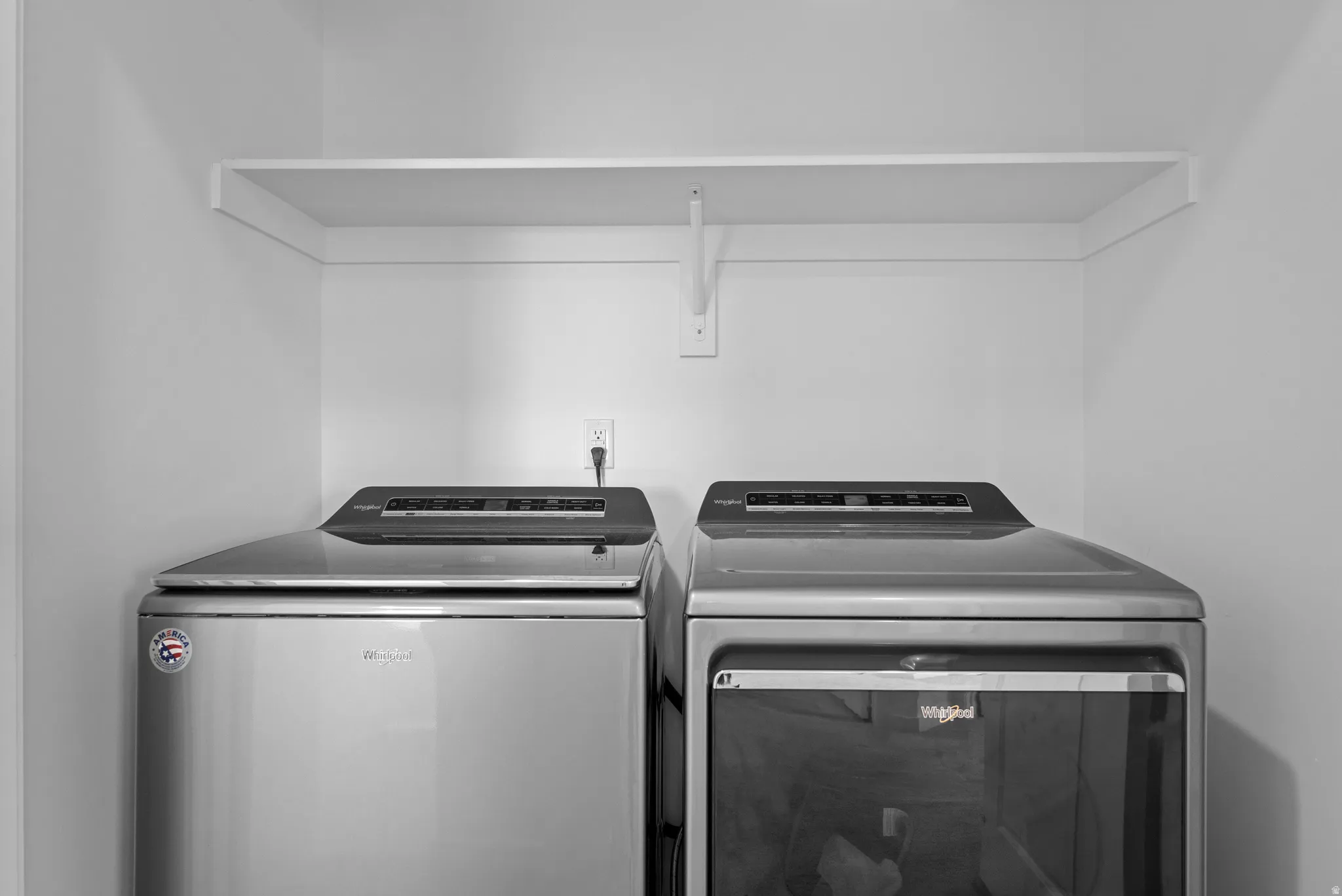 Dedicated laundry space featuring a white built-in shelf, neutral wall tones, and electrical outlets