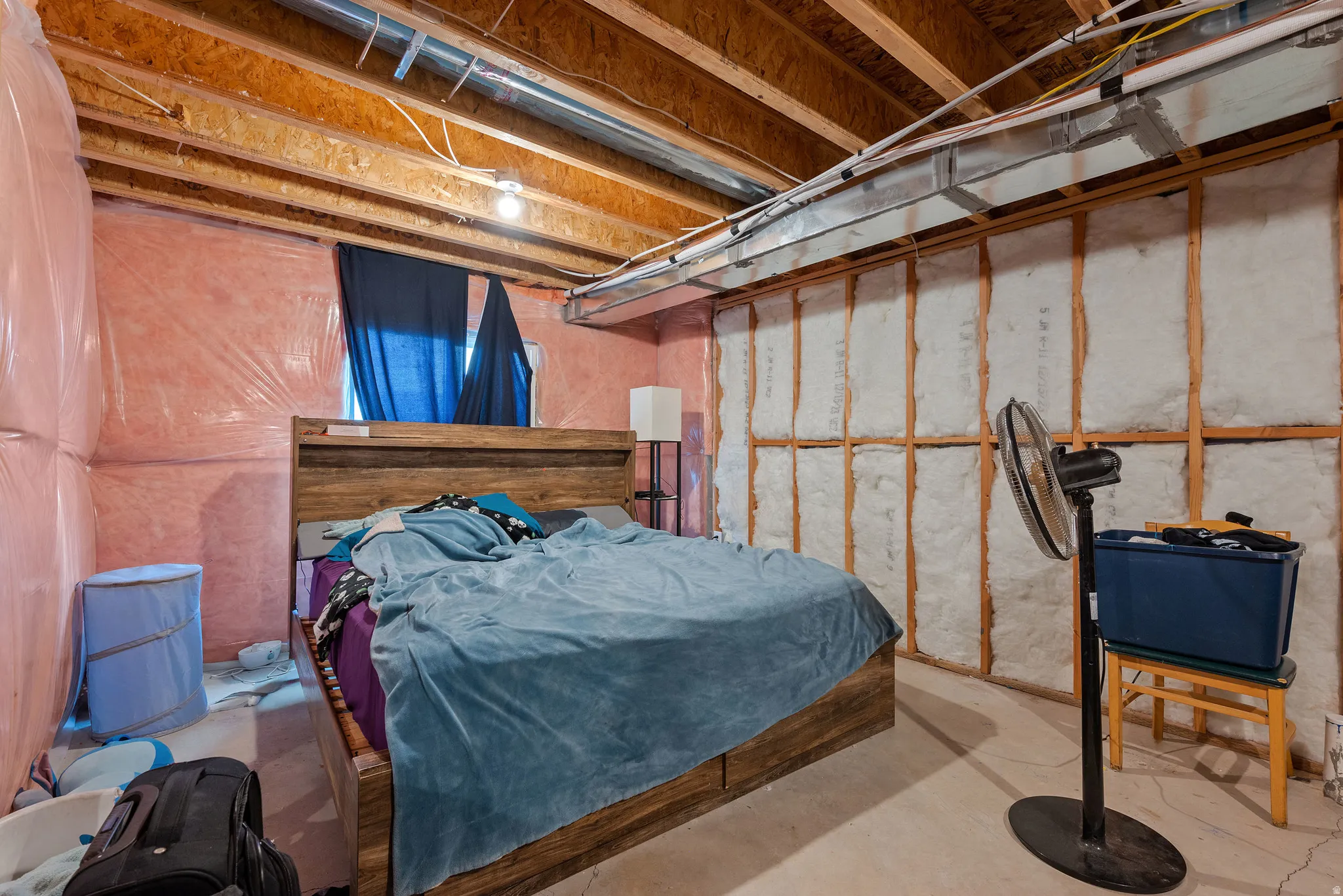 Unfinished basement area featuring exposed wood joists and subflooring, partially insulated walls, and a visible window opening